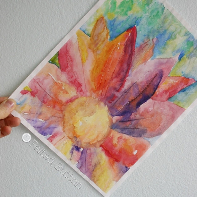 Rainbow watercolor painting of large flower against blue sky, by Susan Carlson of Felted Button | Colorful Crochet Patterns