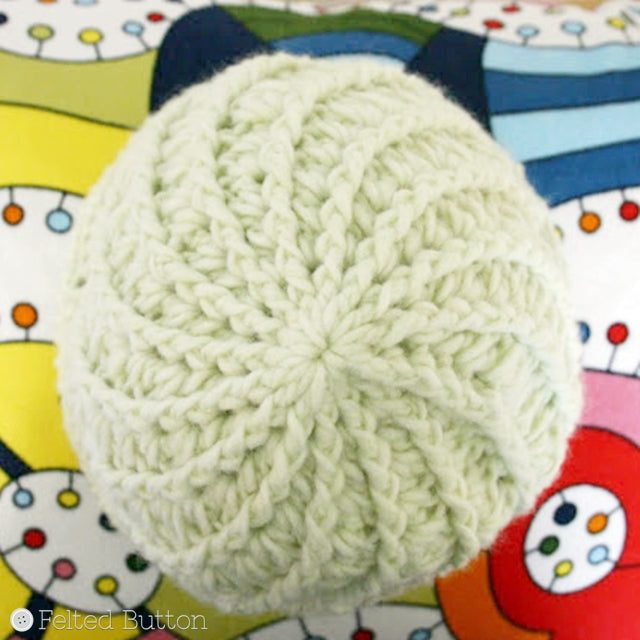 Top view of Divine Hat with swirl and soft green yarn against colorful rainbow background, Susan Carlson of Felted Button | Colorful Crochet Patterns