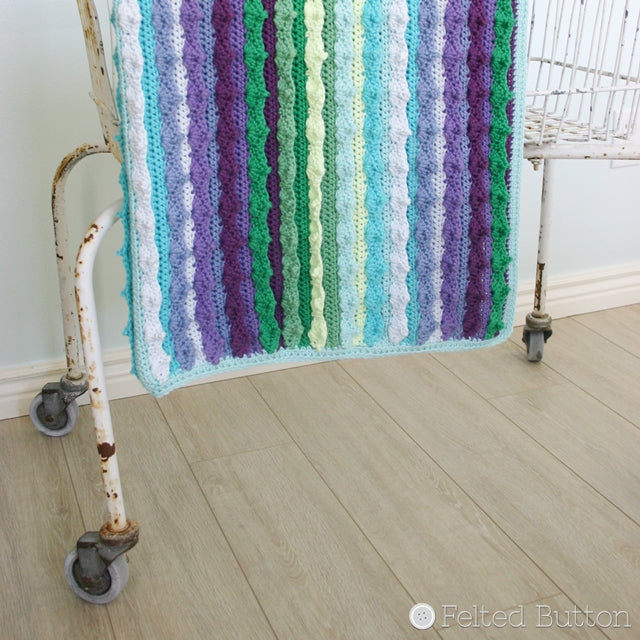 Blue, green and turquoise blanket hanging from basket, Eventide Blanket crochet afghan or throw pattern by Susan Carlson of Felted Button | Colorful Crochet Patterns