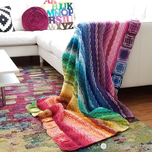 Bright rainbow crochet striped blanket draped over white couch, Every Bit a Blanket, free crochet afghan pattern by Susan Carlson of Felted Button colorful crochet patterns 