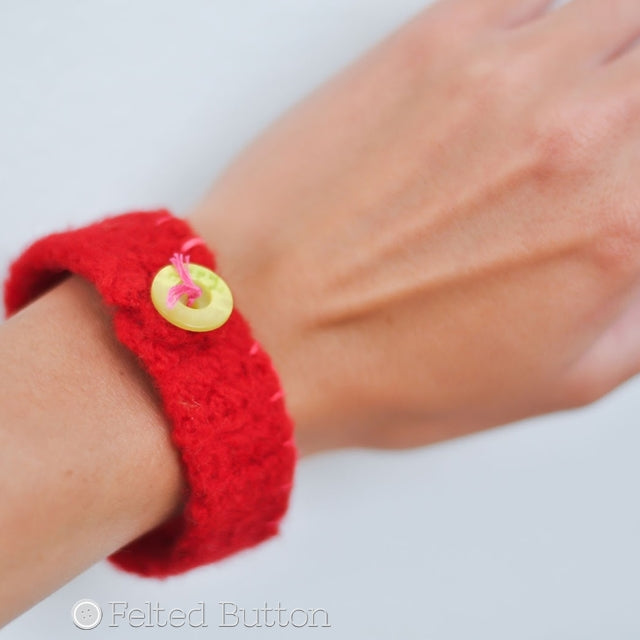 red felted bracelet cuff on wrist with green button and embroidery, Felted Button Bracelet free crochet pattern by Susan Carlson of Felted Button | Colorful Crochet Patterns