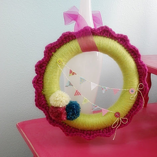 Yarn wrapped wreath in yellow-green and pink with ribbons, pom poms and bunting, by Susan Carlson of Felted Button | Colorful Crochet Patterns