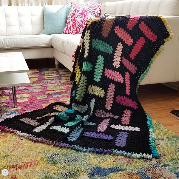 Rainbow of crochet granny rectangles that look like they are woven against a black background with pom edging, Warp and Weft free crochet patter by Susan Carlson of Felted Button
